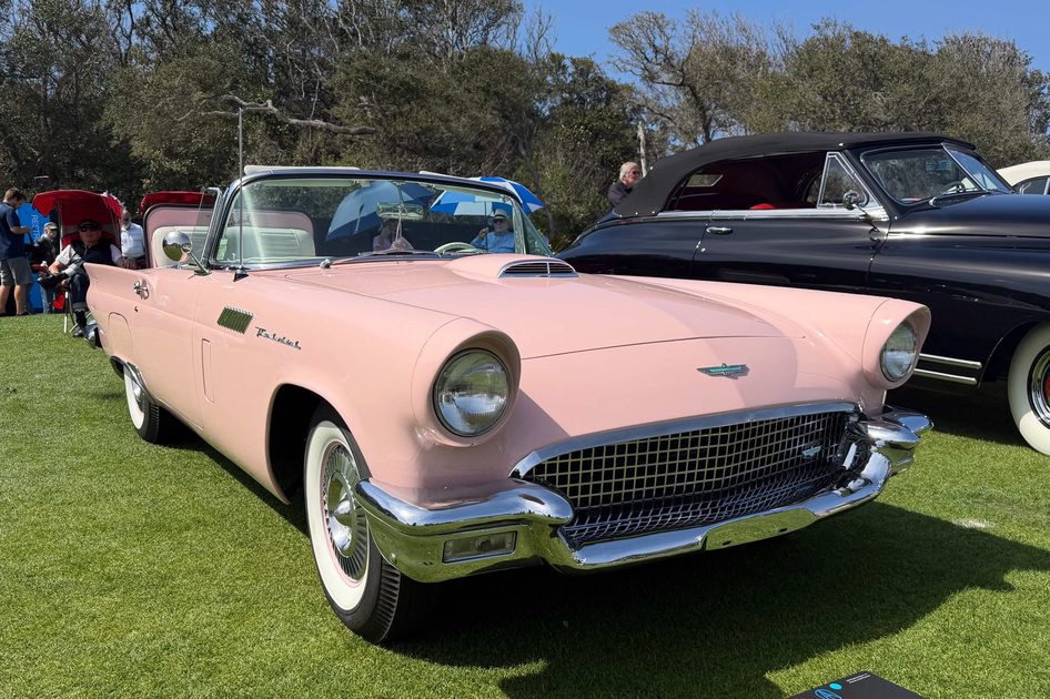 a classic pink 1957 ford thunderbird car displayed on a grassy area