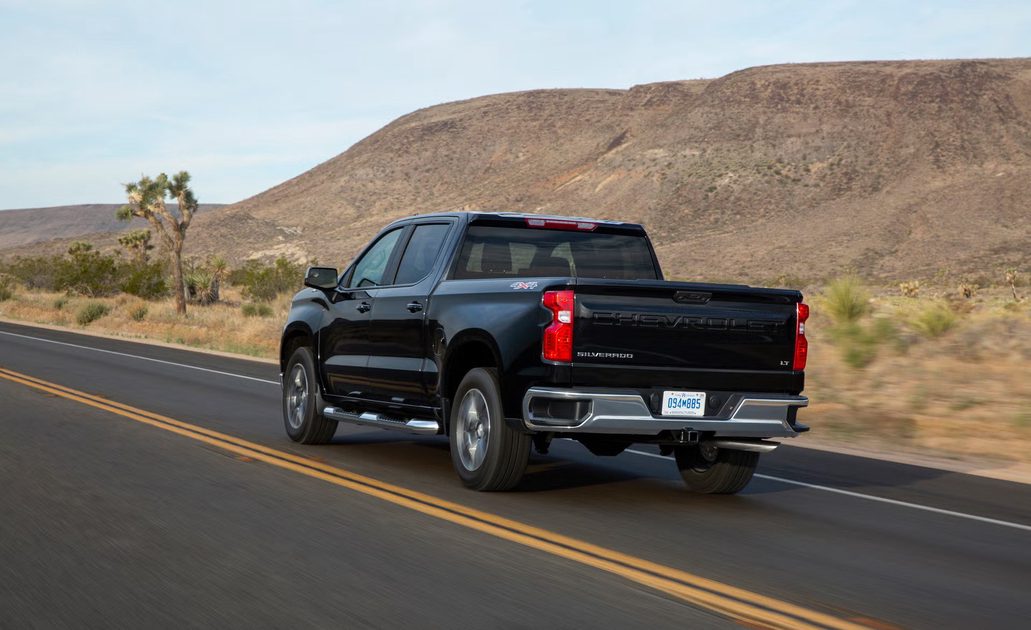 rear three quarter view of black chevrolet pickup driving on desert highway near rocky hills.